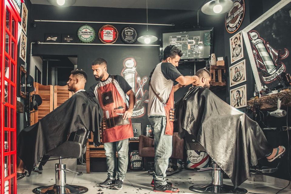 Two barbers mid-cut in a busy shop, no hands free for the phone